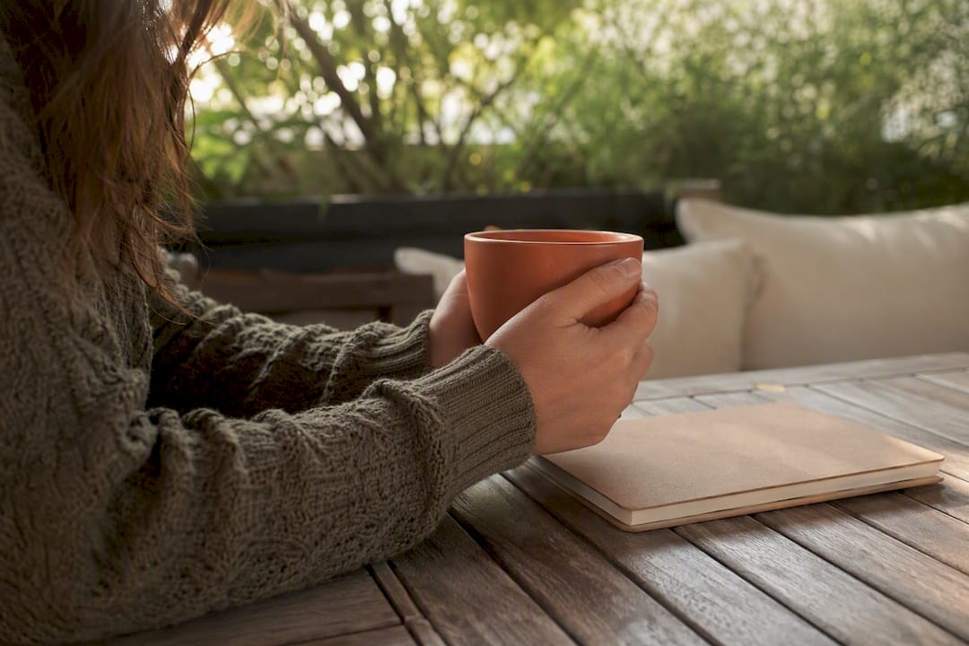 Hands holding mug beside personal journal