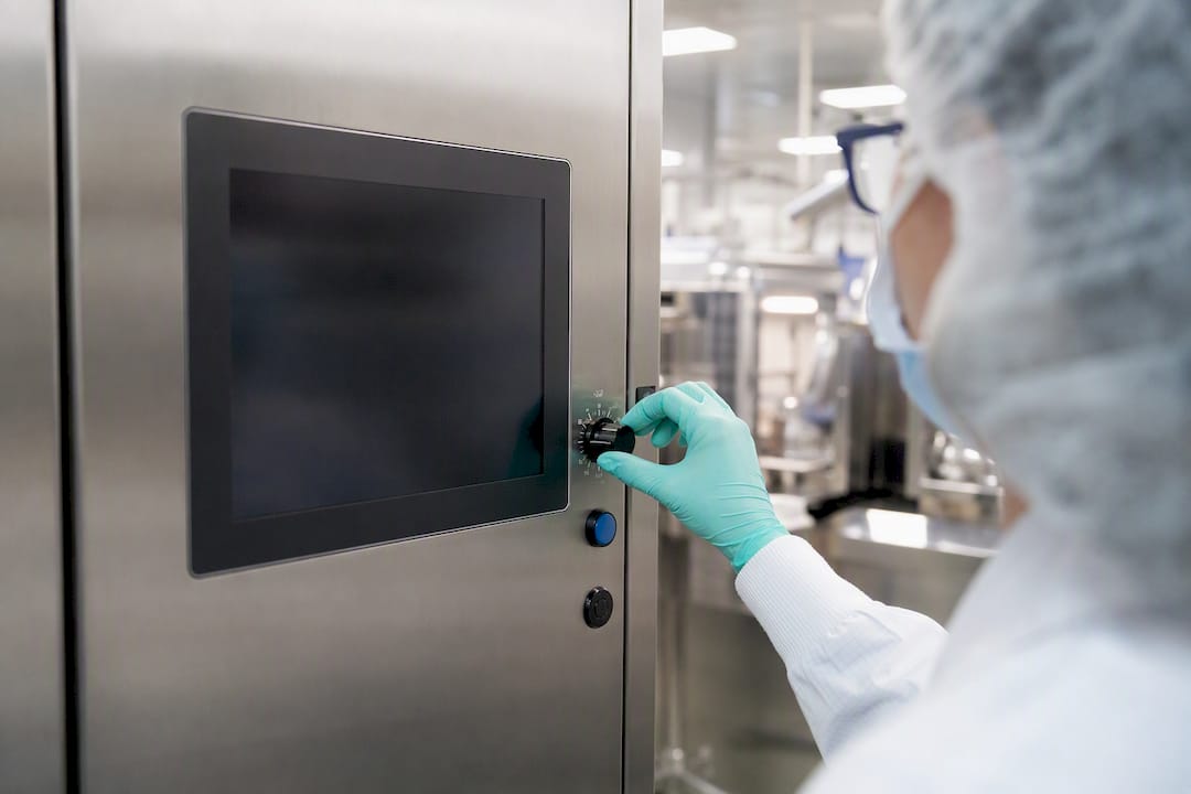 Gloved hand pressing control panel in biotech lab
