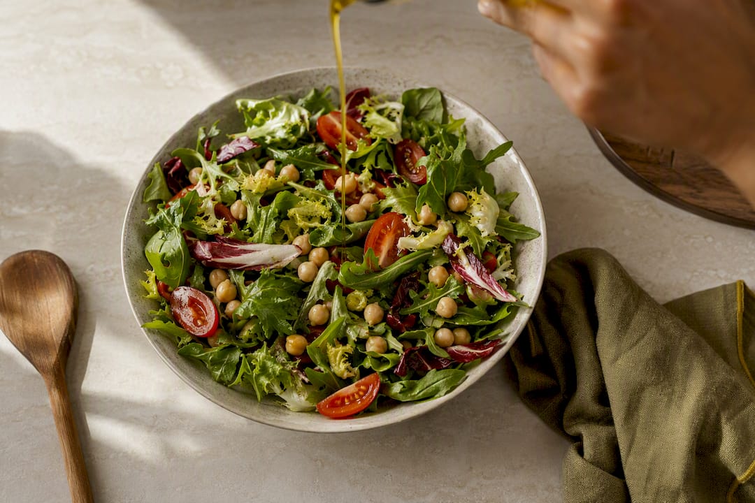 Mano aderezando una ensalada mediterránea con AOVE