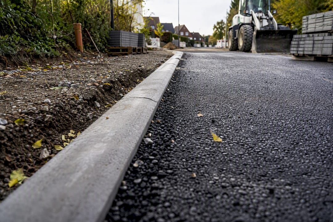 Detailaufnahme des Asphaltfräsens am Bordstein mit darunterliegenden Schichten