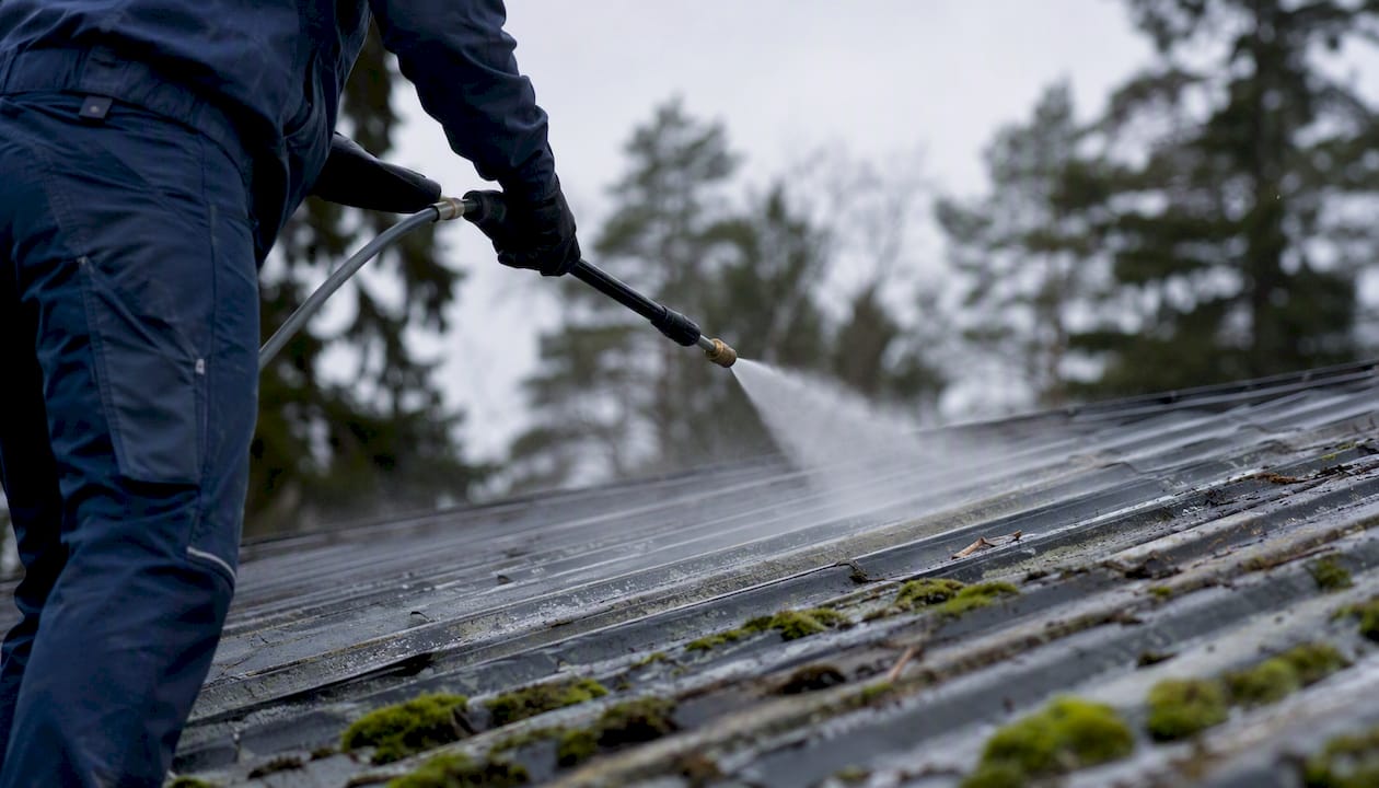 Soft-wash spray on metal roof on cloudy day