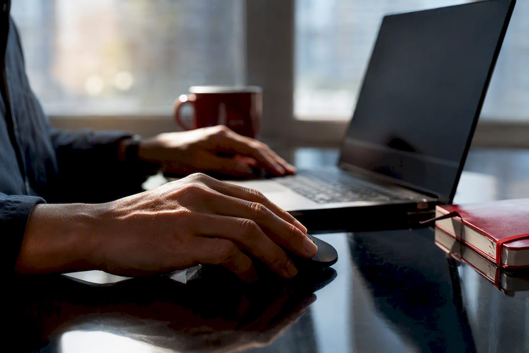 Hands clicking mouse near closed laptop on black desk