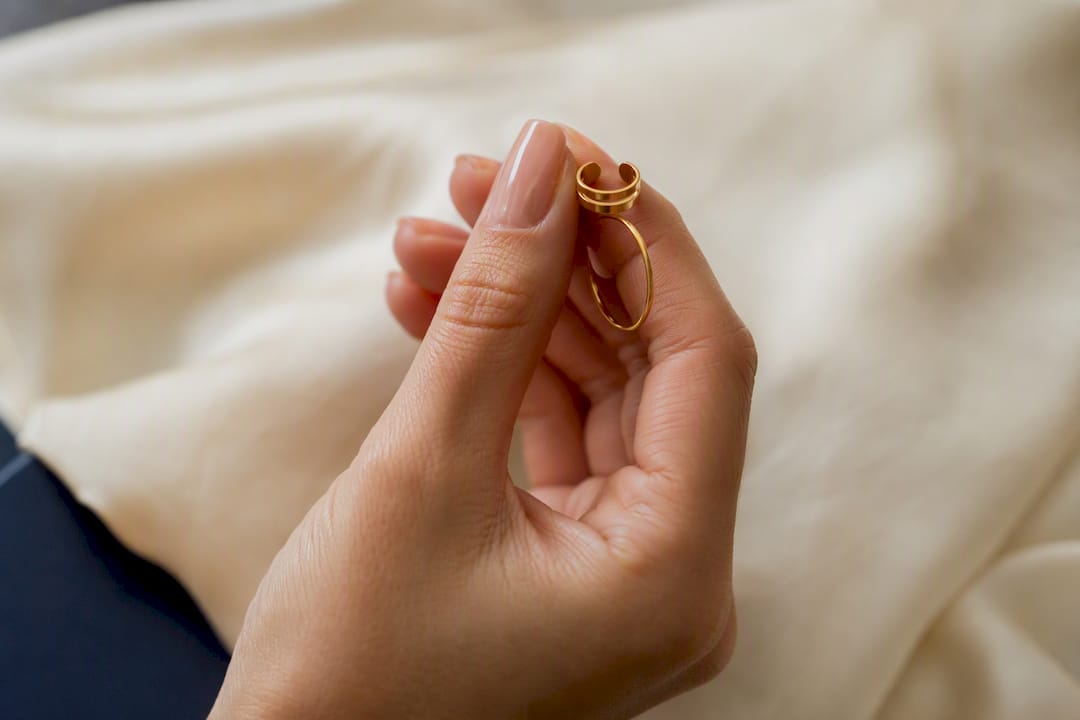 Minimal gold ear cuff and nose ring on cream fabric
