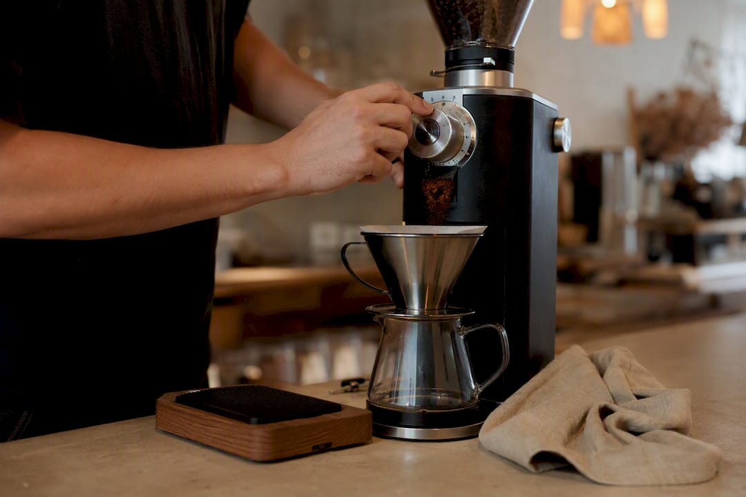 Hands setting grinder and pouring ground coffee