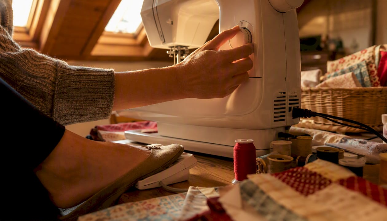 Hands adjusting tension dial on sewing machine