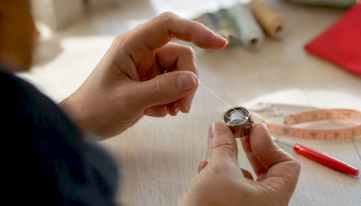 Hands checking bobbin tension in sewing machine
