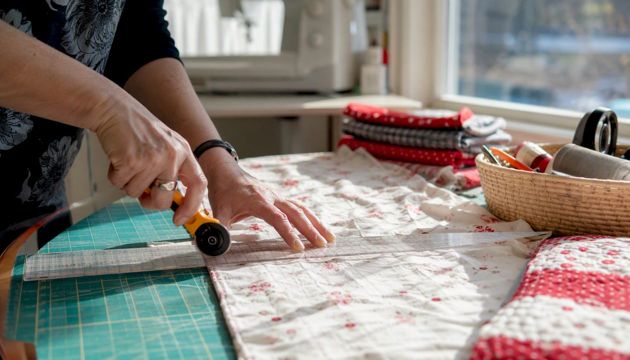 Hands cutting fabric strips with long quilting ruler