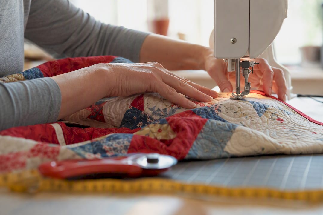Hands maneuvering quilt fabric through sewing machine throat
