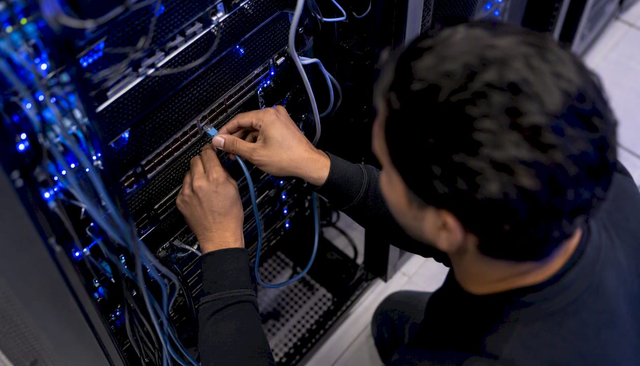 Hands plugging network cable into server rack