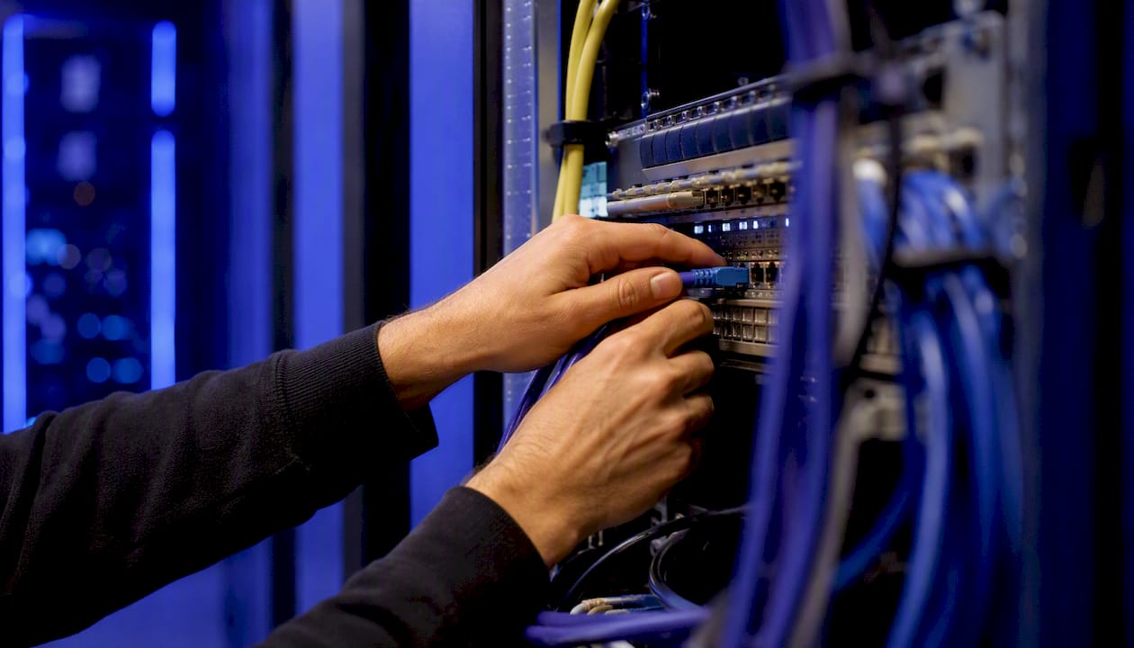 Hands plugging network cable into server rack port