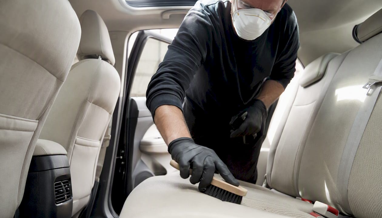 Person scrubbing car seat wearing N95 mask and gloves