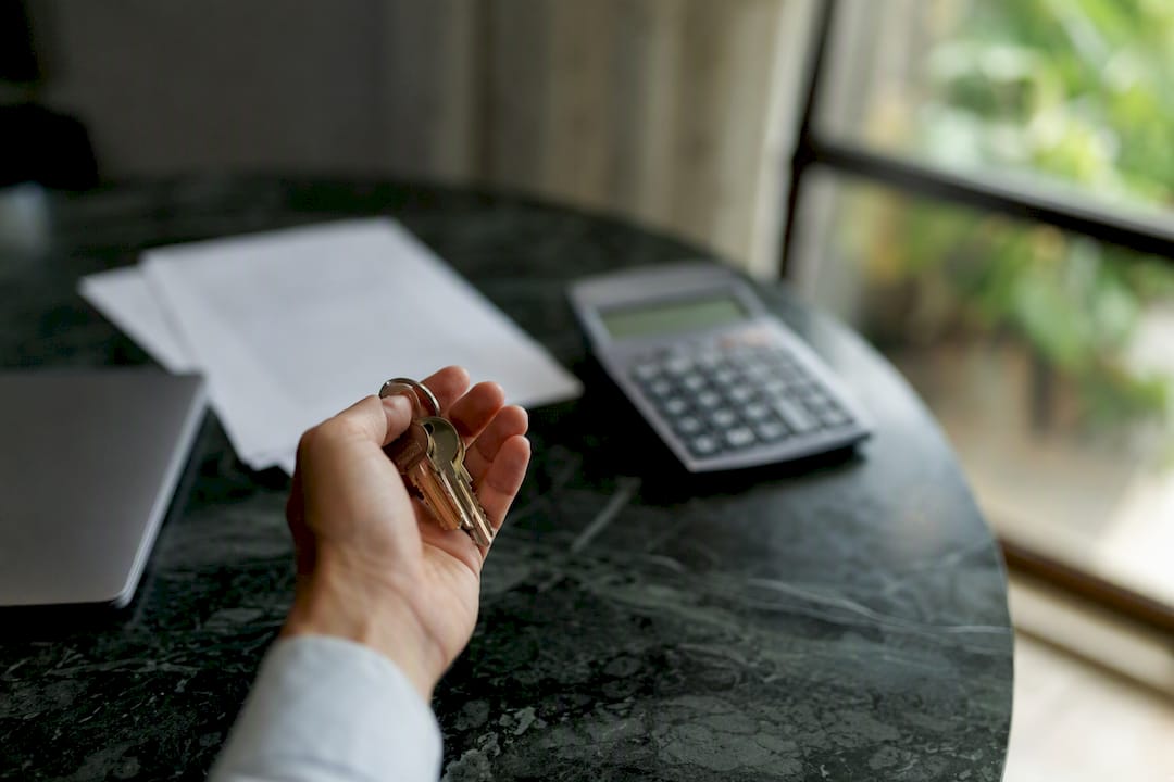 Una mano sostiene unas llaves de casa junto a una calculadora