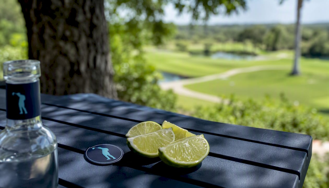 Vodka bottle neck with golf ball marker and lime wedges