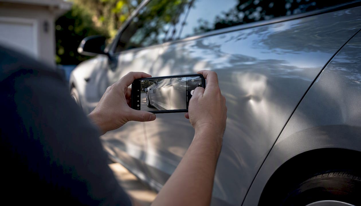Hands taking photos of dent on car panel