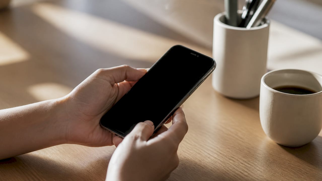 Un paio di mani che tengono uno smartphone poggiato su un tavolo di legno