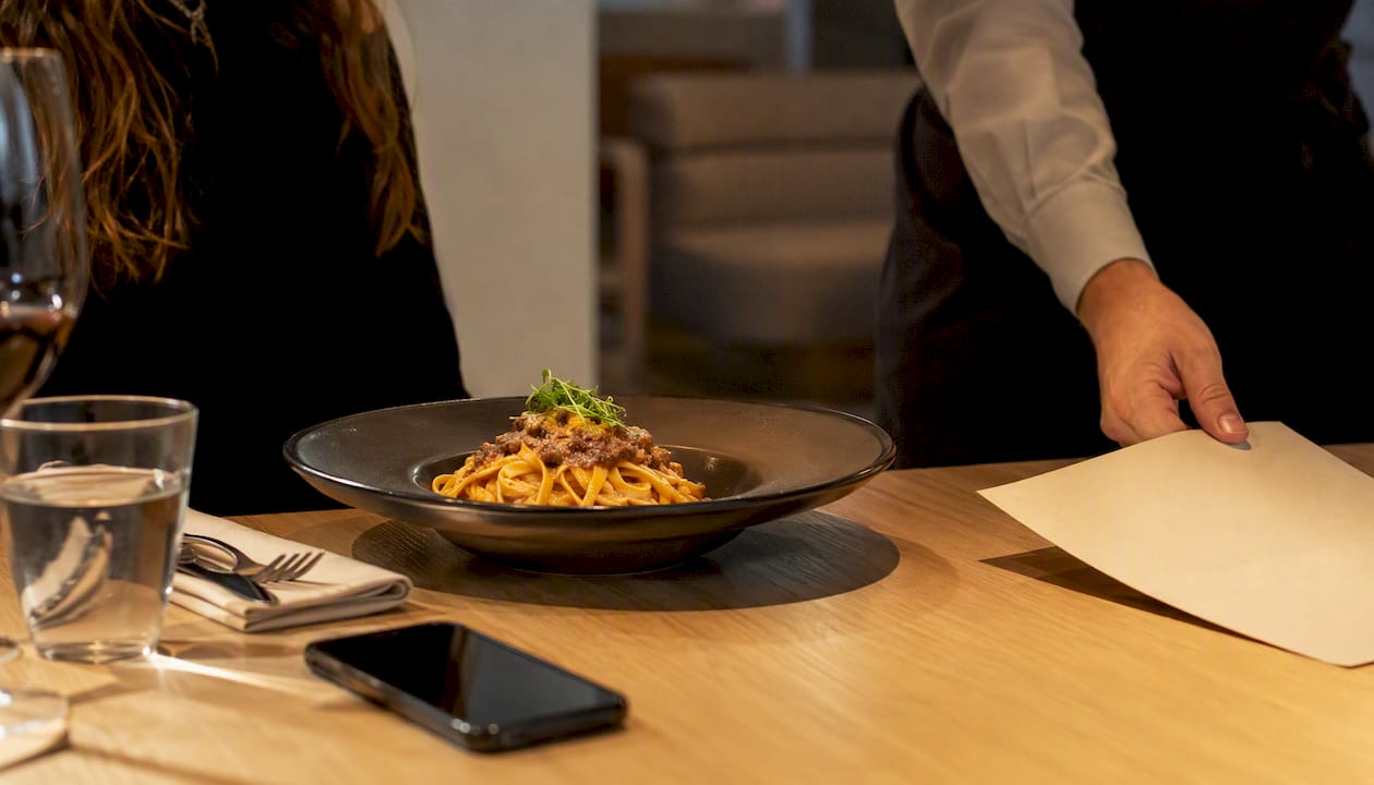 Un bel piatto di pasta appena servito, con lo smartphone rigorosamente a faccia in giù sul tavolo.