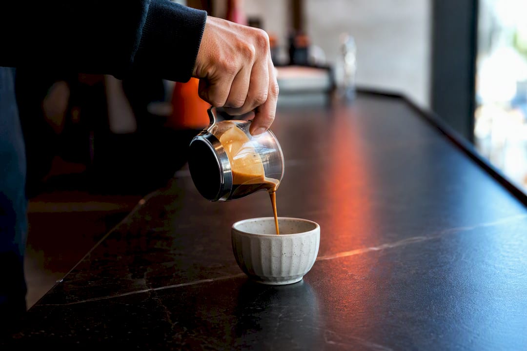Una mano versa lentamente l’espresso sul bancone del bar, creando quel profumo intenso che solo il caffè appena fatto sa regalare.
