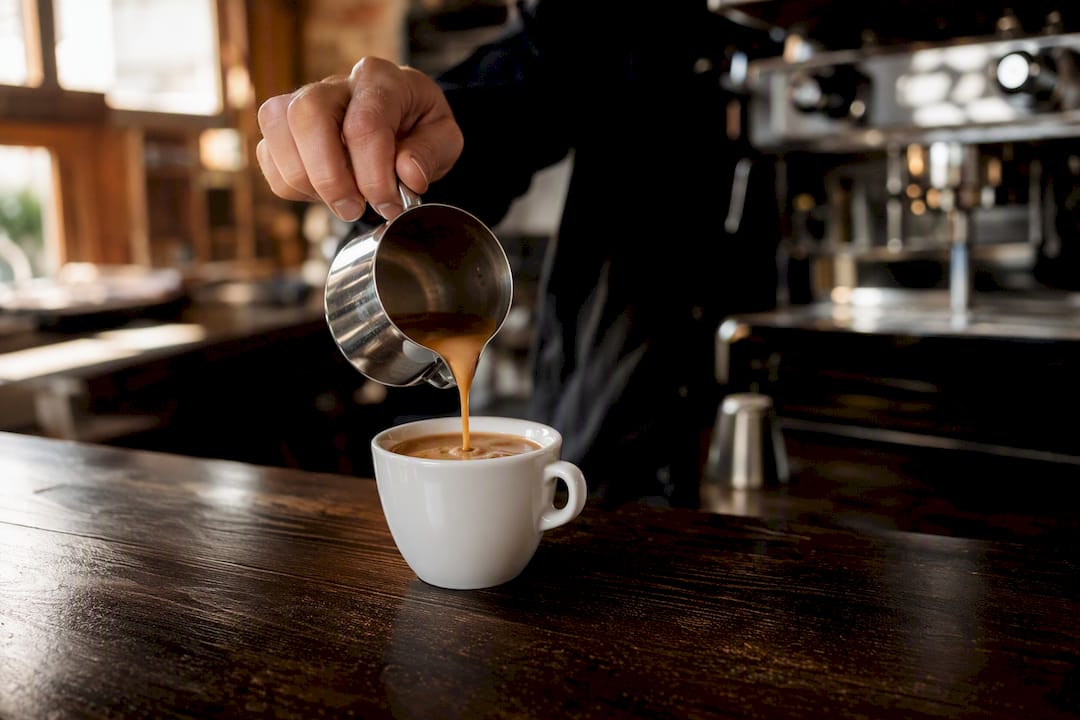 Mano che versa un caffè espresso in una tazza di ceramica