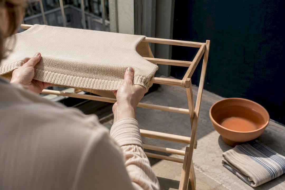 Hands air-drying knitwear on wooden rack