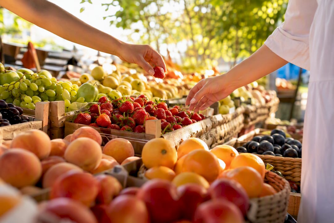 Fresh fruit display with shoppers' hands selecting fruit