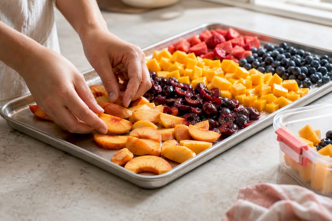 Hands arranging sliced fruit for freezing