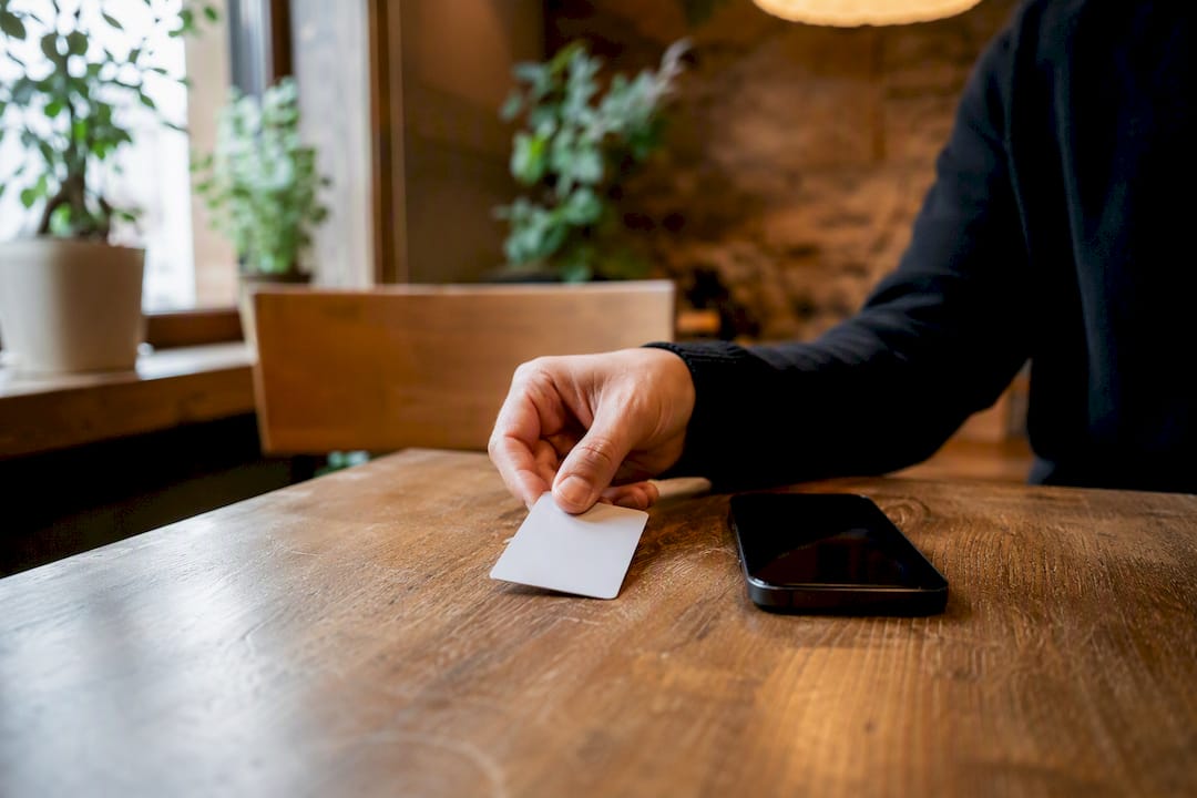 Hand legt NFC-Karte neben Smartphone auf den Tresen
