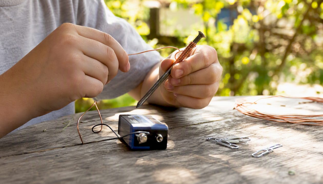 Child hands wrapping wire around nail for electromagnet