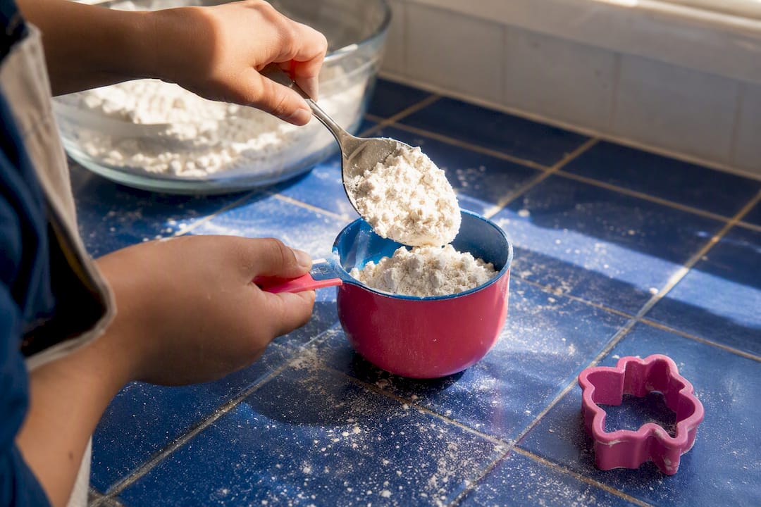 Hands spooning flour into dry measuring cup