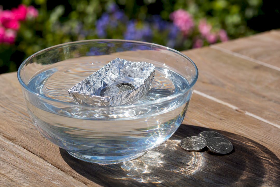 Aluminum foil boat floating on water with pennies