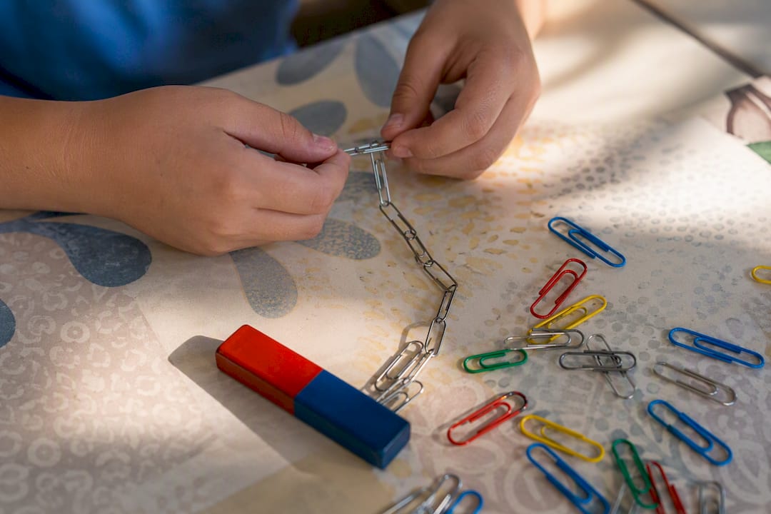 Hands building paperclip chain near magnet