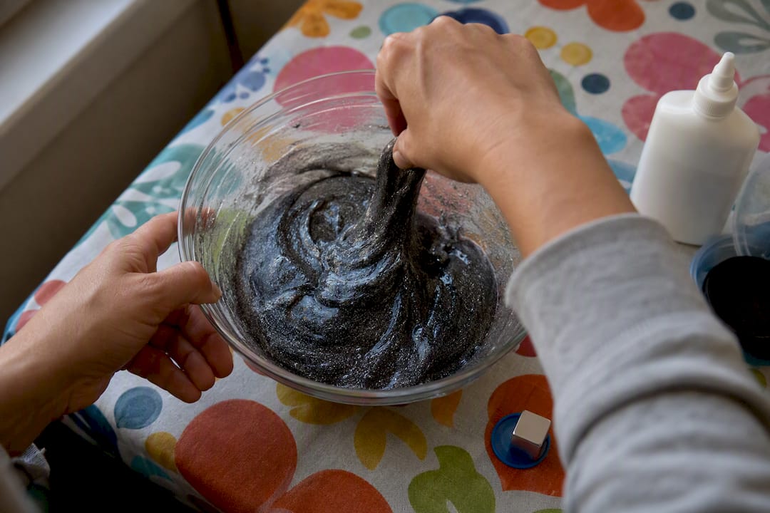 Adult hands mixing iron oxide magnetic slime