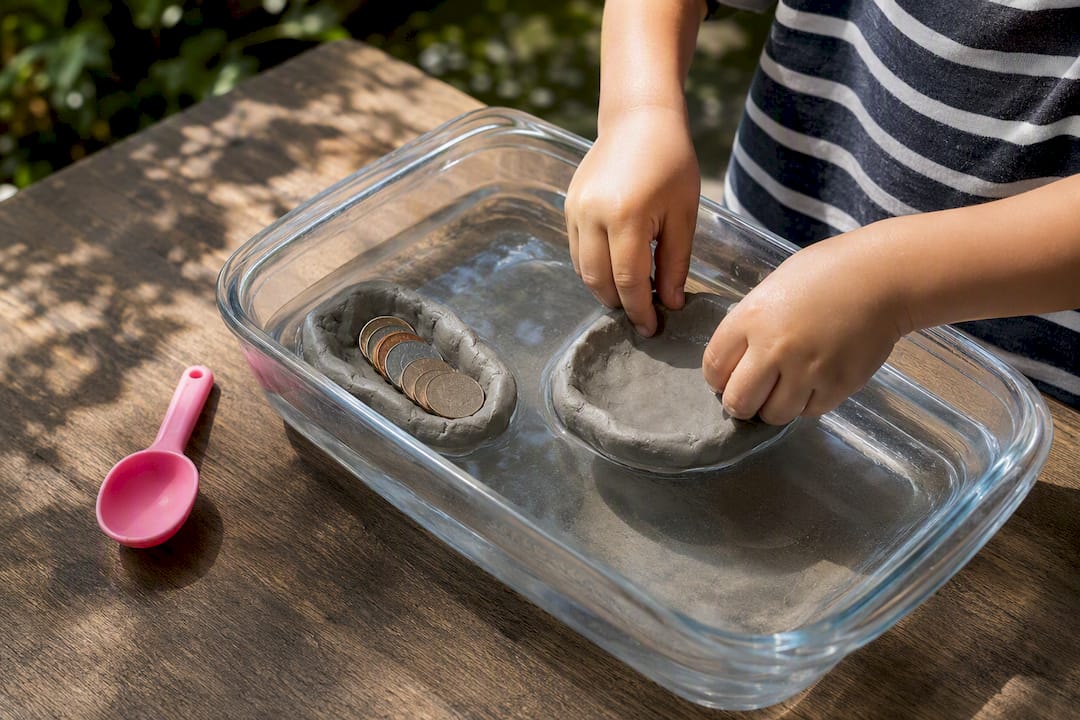 Child testing a clay raft with coins