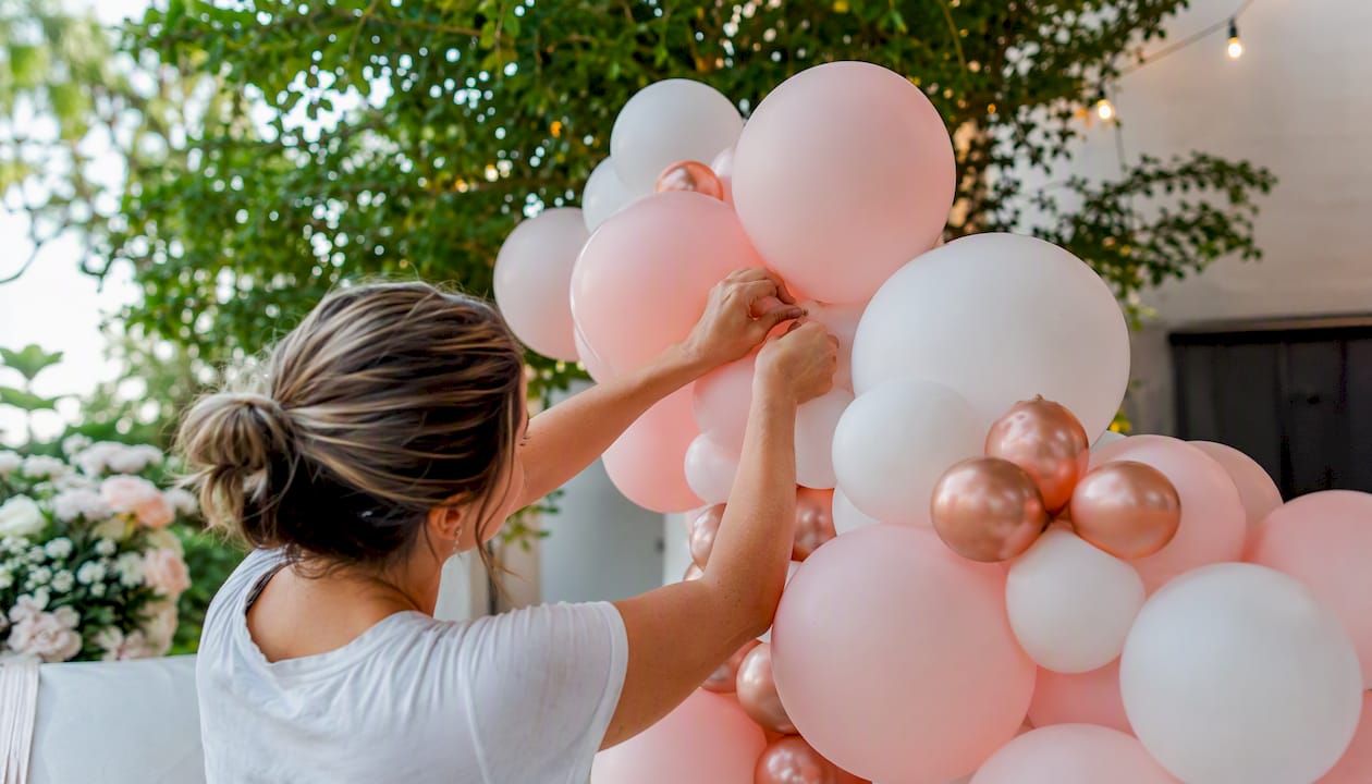 Hands assembling blush pink rose gold balloon arch