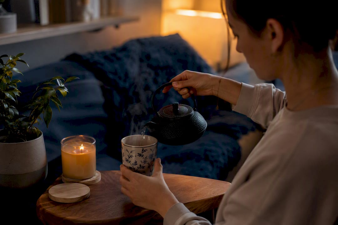 Hands pouring tea beside candle and habit tracker