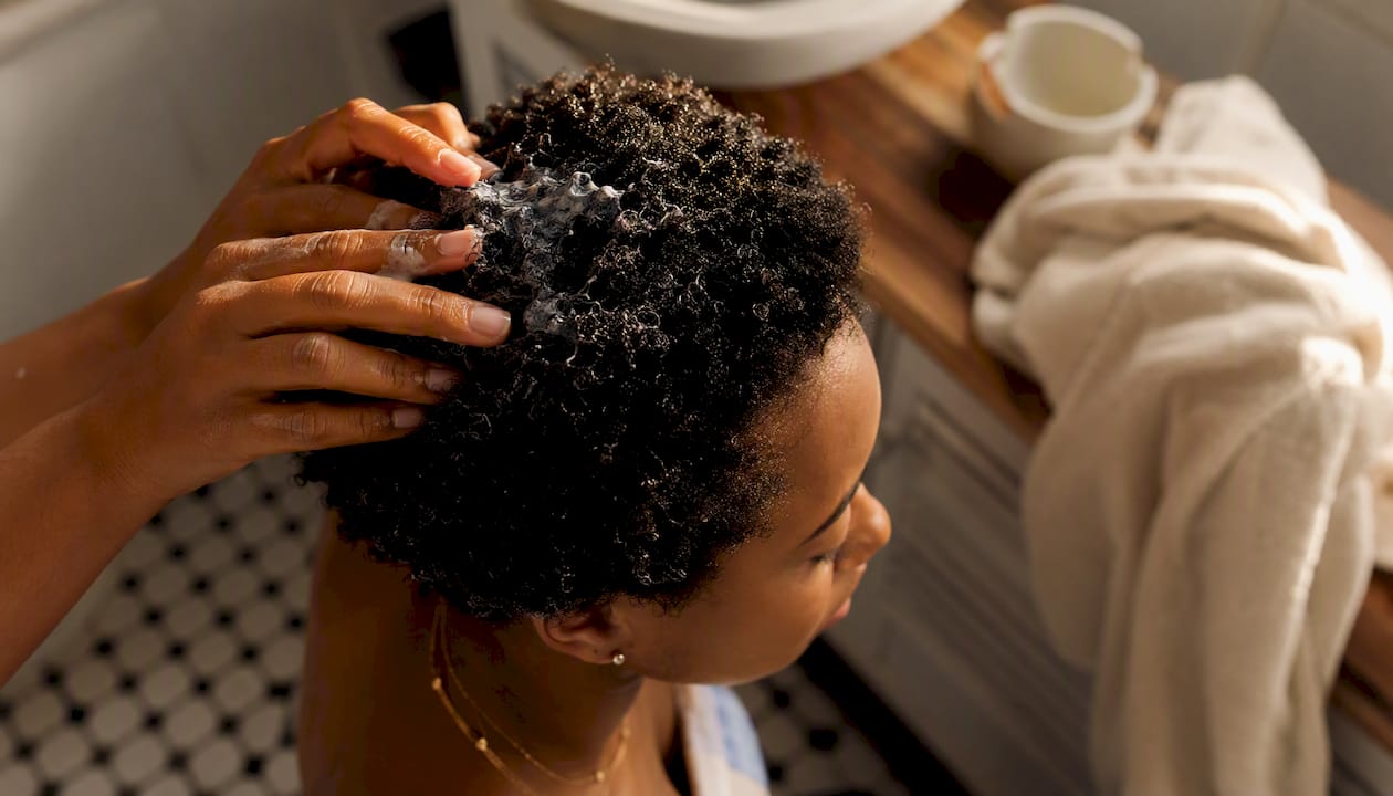 Hands scrunching curl custard into short coily hair