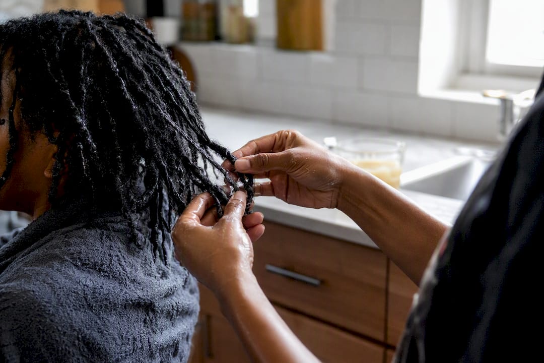 Hands removing faux locs with conditioner soak