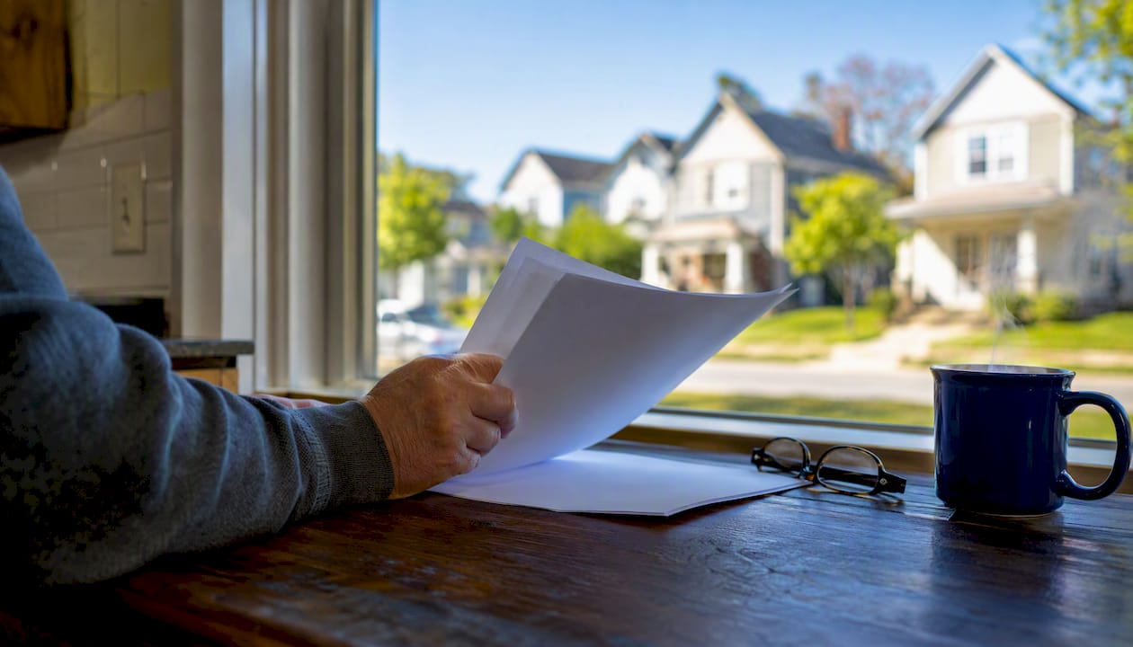 Hand holding landlord insurance document near rental home