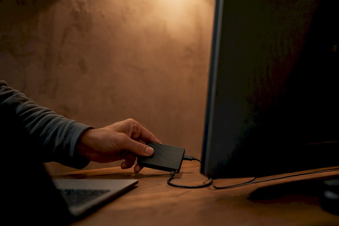 Hand holding external drive near monitor