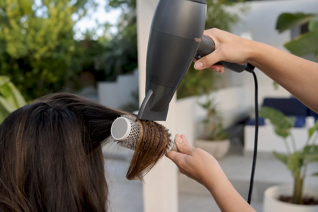 Hands styling hair with round brush and dryer