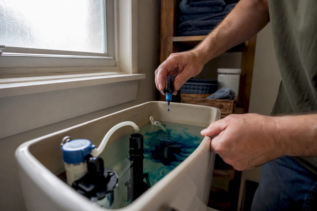 Hands adding food coloring to toilet tank