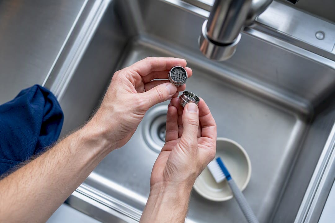 Hands cleaning a household faucet aerator