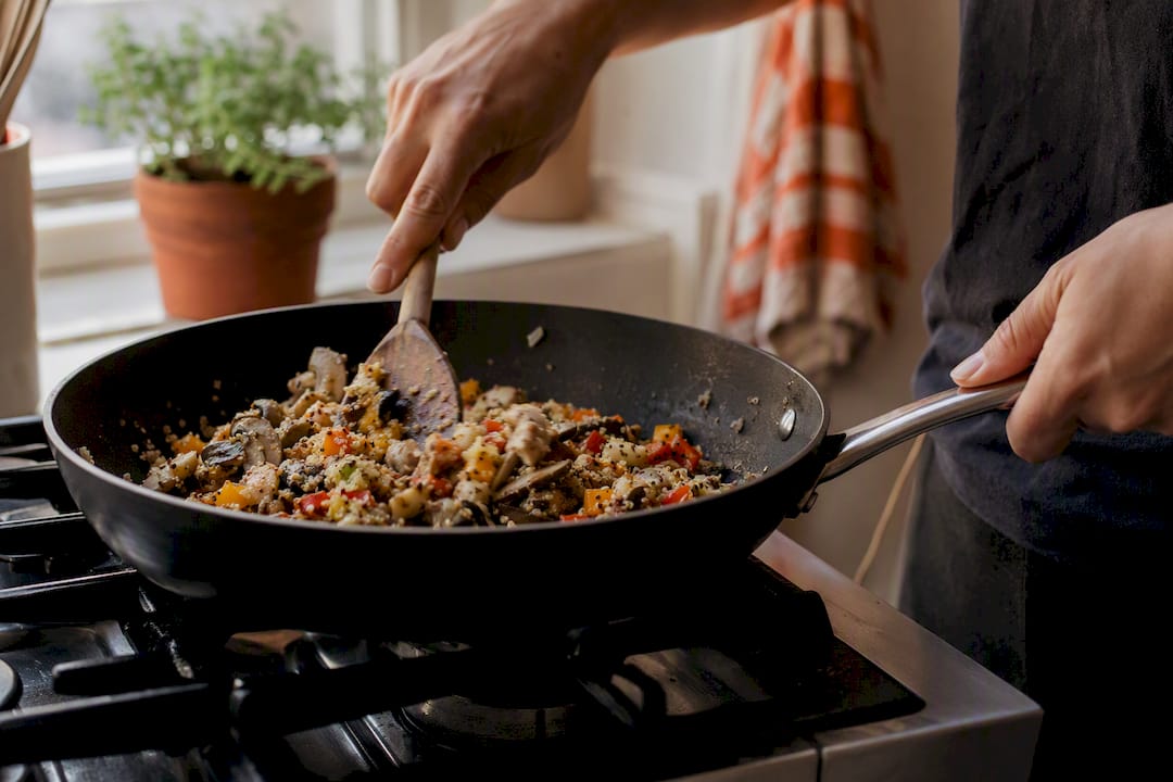 Hands stirring leftover meal in skillet
