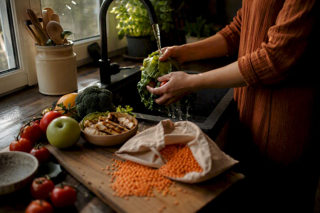 Hands rinsing fresh vegetables in kitchen sink