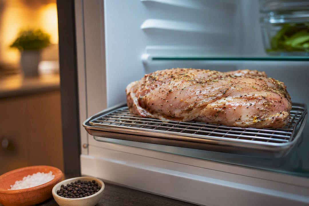 Seasoned chicken resting uncovered in refrigerator