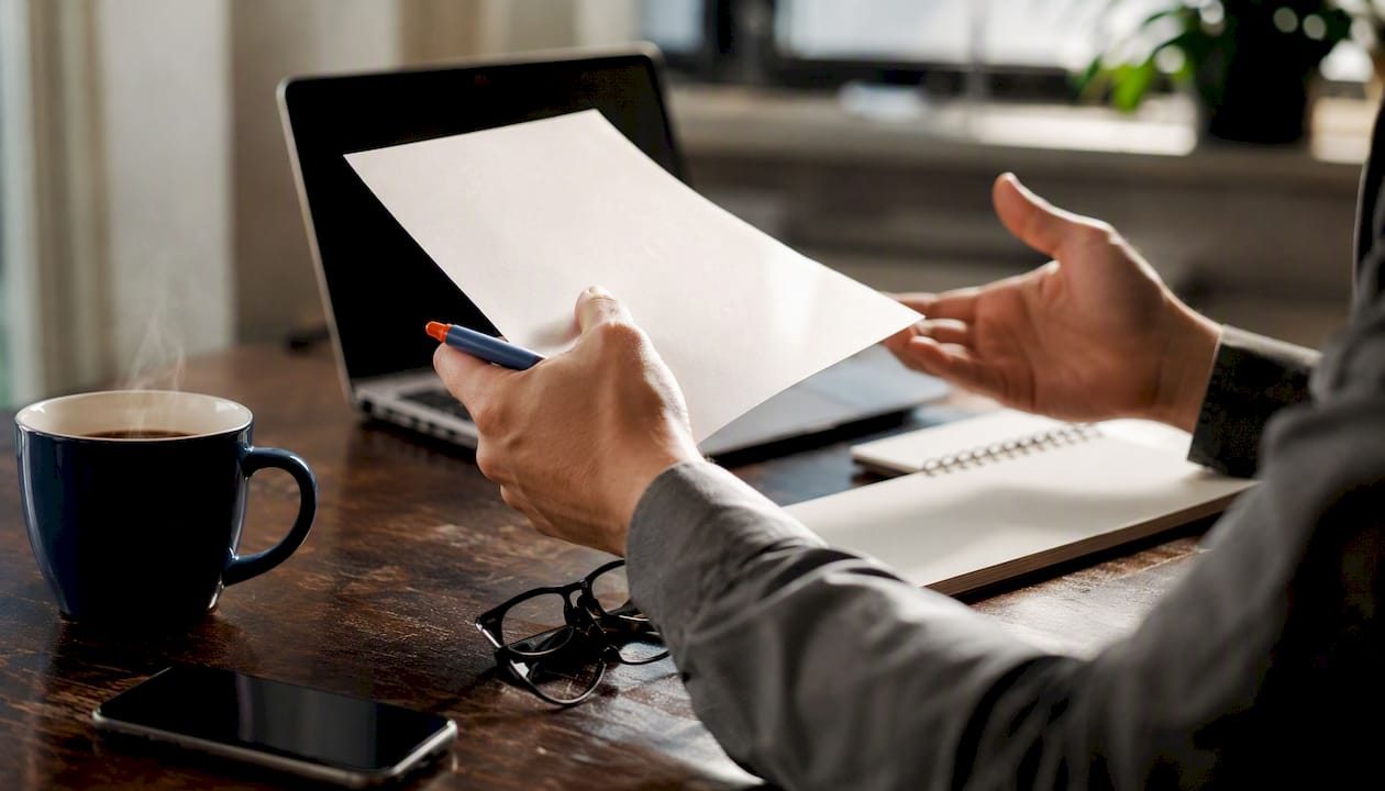 Hands reviewing notes beside a dark laptop screen