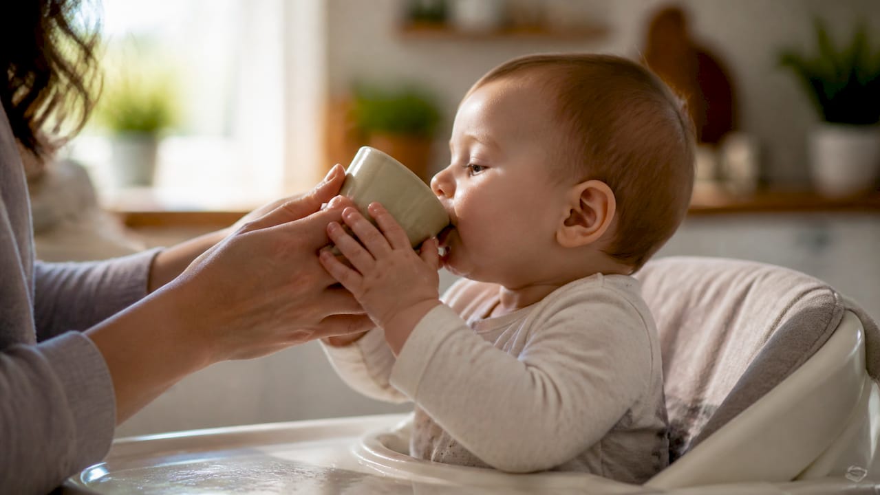 Parent hand guiding baby's hands on cup