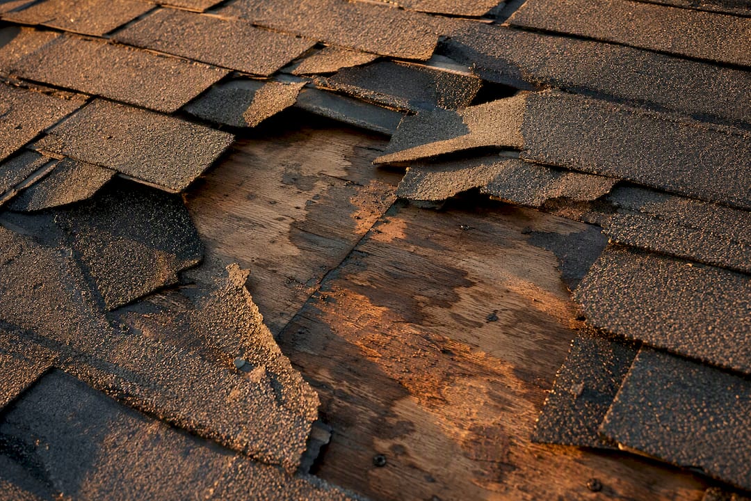 Close-up of damaged shingles and weathered roof section