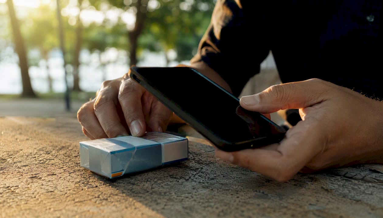 Hands holding phone near cigarette pack edge