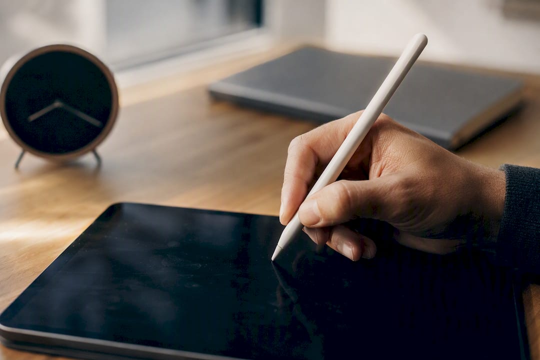 Une main tient un stylet, prête à écrire sur une tablette.