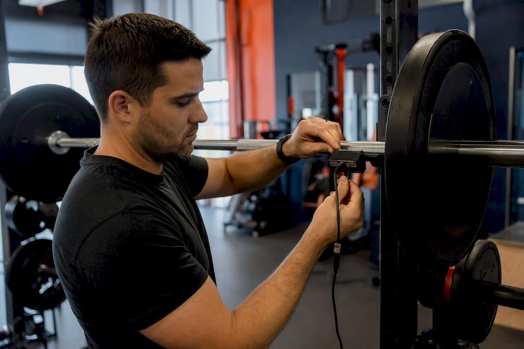Coach attaching velocity device to barbell